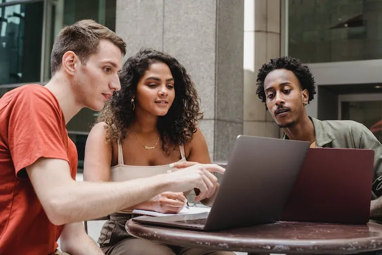 Two men and one woman all casually dressed look at a laptoip