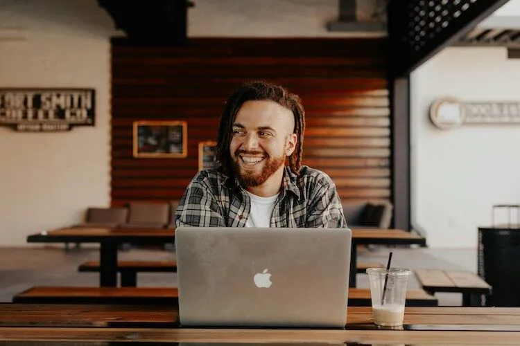 Guy with red beard smiles over the top of Apple laptop