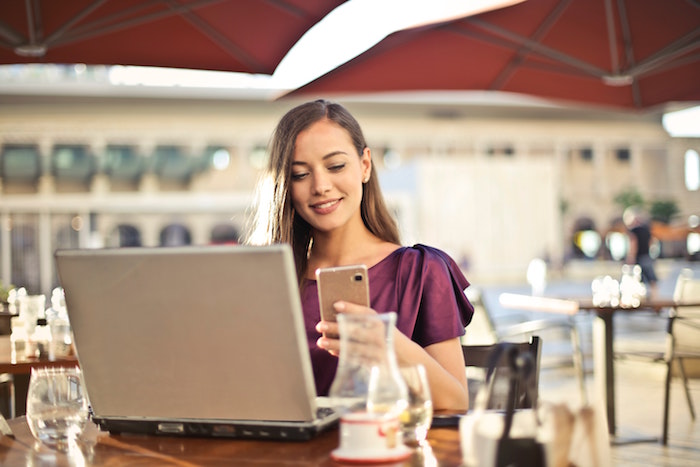 Woman smiles at open laptop while holding a mobile and checking LinkedIn