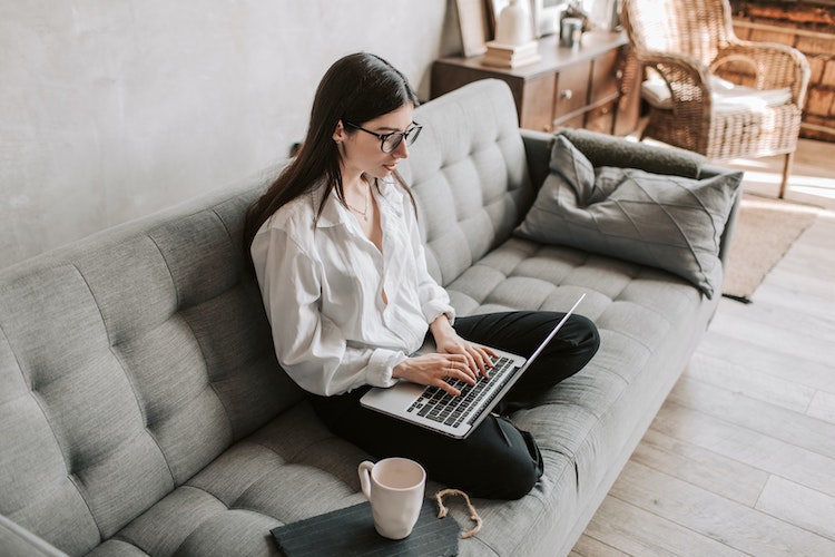 Cross legged woman sits on sofa with laptop