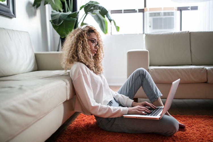 Woman with blonde curly sits on the floor in front of her laptop