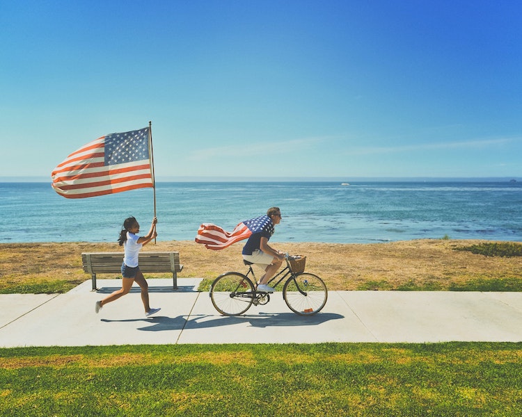 Person on bike followed by runner holding USA flag