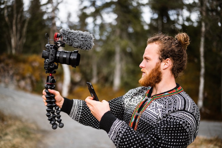 red haired man holds camera and mic and records himself