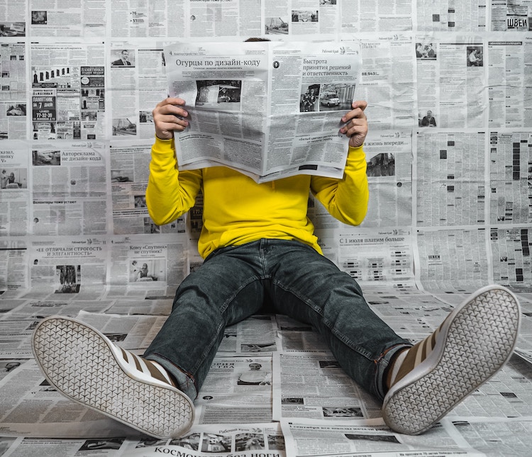man in yellow tee reading a newspaper in a room papered with newspapers