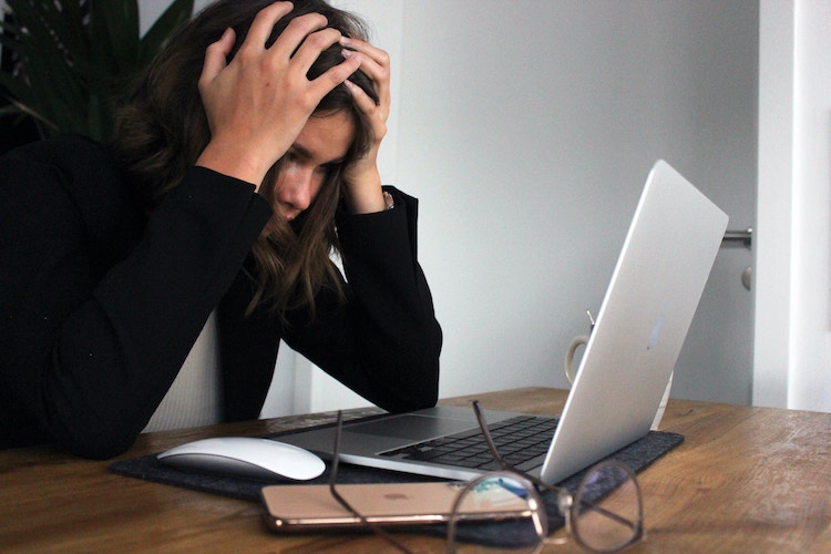 Woman holds her head in front of laptop