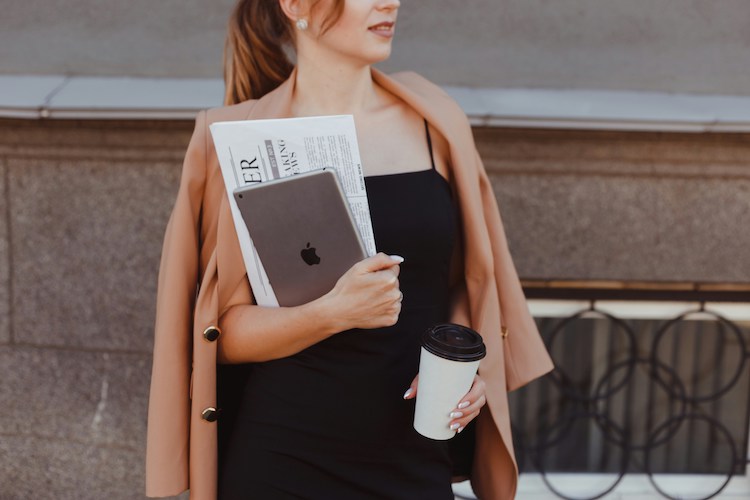 legant white woman carries laptop and coffee cup
